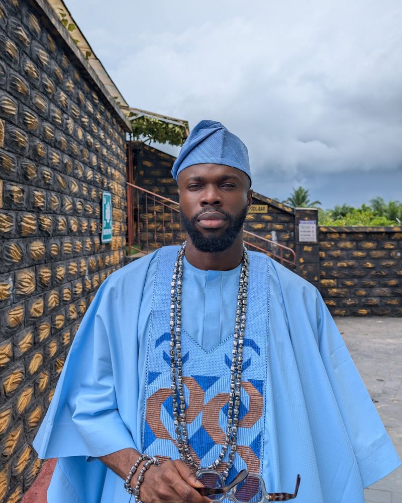 Sky in a light blue agbada and cap, standing outside